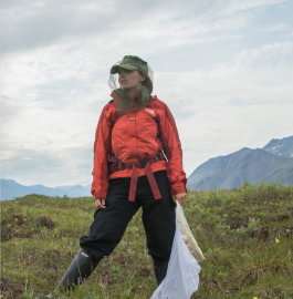 Hollis Woodard stands in a beekeeping hat outside in nature